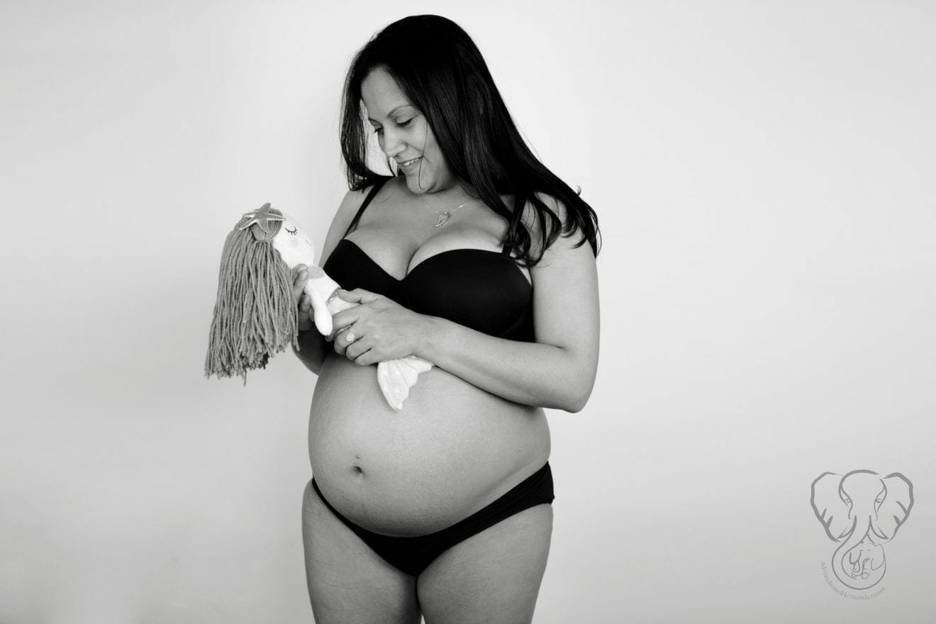 Black and white photo of Miranda and Peanut's Mermaid. Miranda is wearing black undergarments and is smiling down at the mermaid in her hand. (4th Trimester Bodies Project)