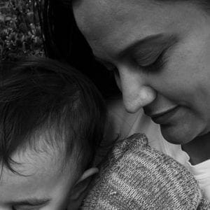 Close up of mother holding toddler and stuffed elephant. Mother's eyes are closed and is facing down. Only the top left half of the toddler's face is visible.